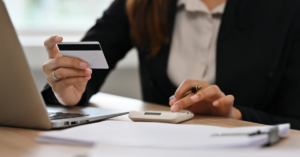 a woman sitting at a desk with a calculator and credit card raised in one hand.
